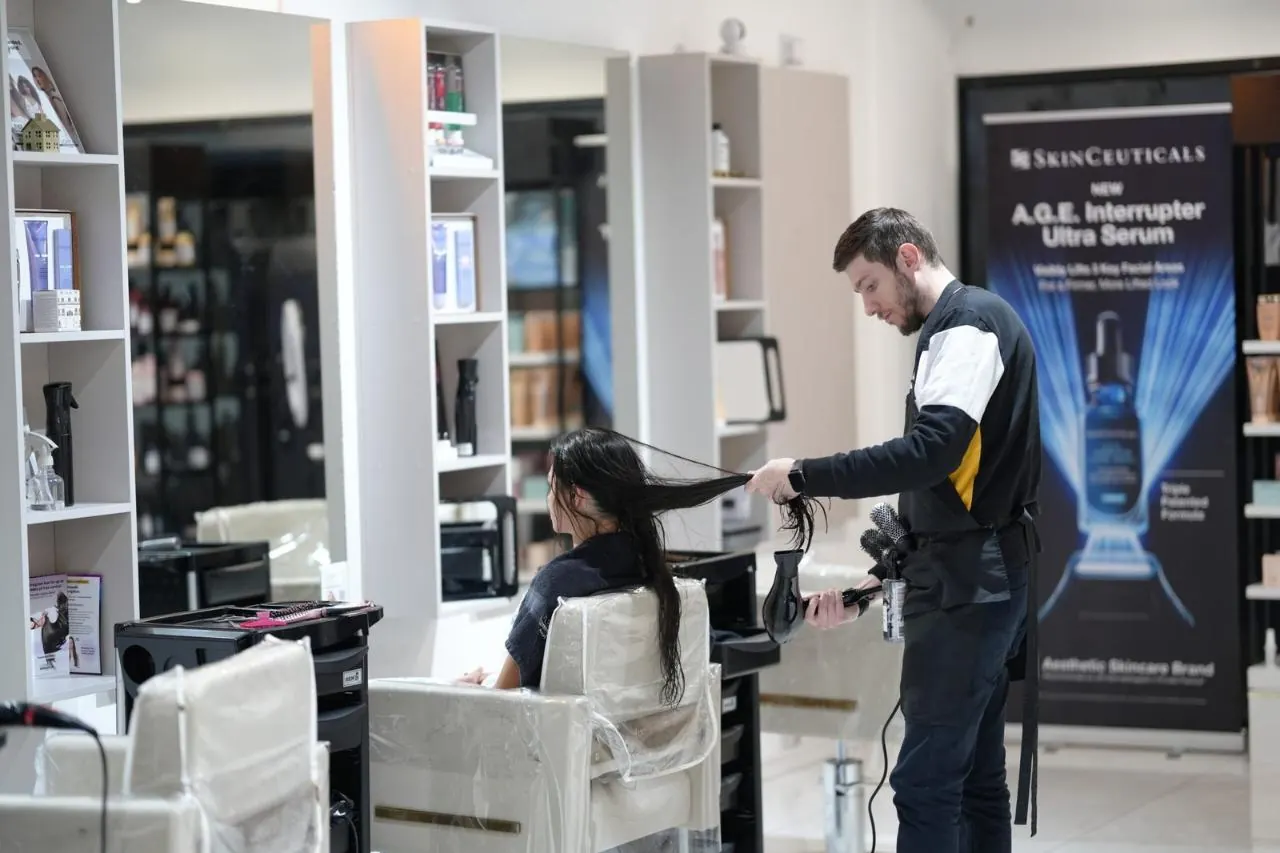 A stylist finishing a client's hair beside the product shelves